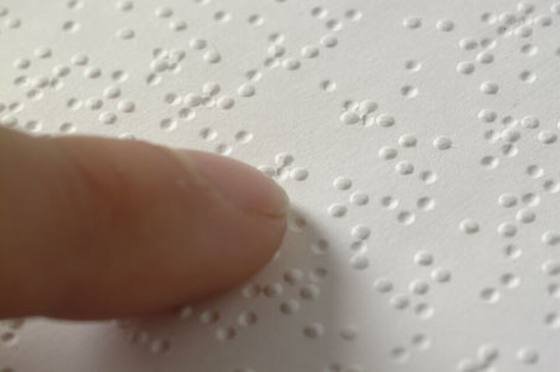 Close-up of a fingertip resting on a page of embossed braille dots