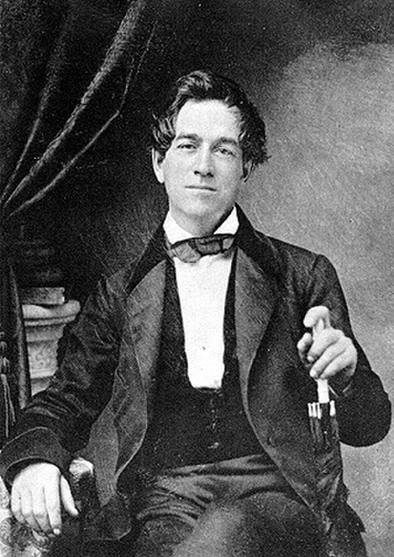 Black-and-white photograph of a young Alfred Vail seated in a dark velvet jacket, holding a small object in one hand