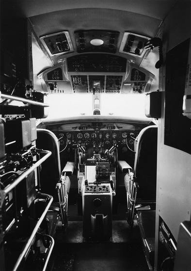 Black-and-white photo looking forward through the flight deck of a 1950s Convair airliner with two pilot seats, instrument panels and radio equipment racks