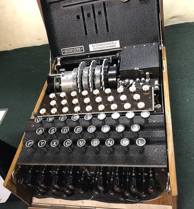 An Enigma machine in its wooden case with the lid open, showing the rotors at the top, the lampboard, the keyboard and the plugboard at the front