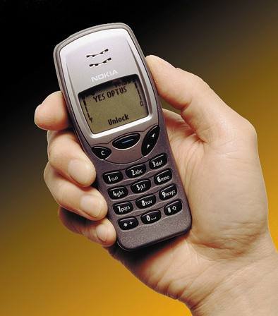 A hand holding a Nokia 3210 mobile phone, showing its small monochrome screen and a 12-key keypad with letters printed on the number keys