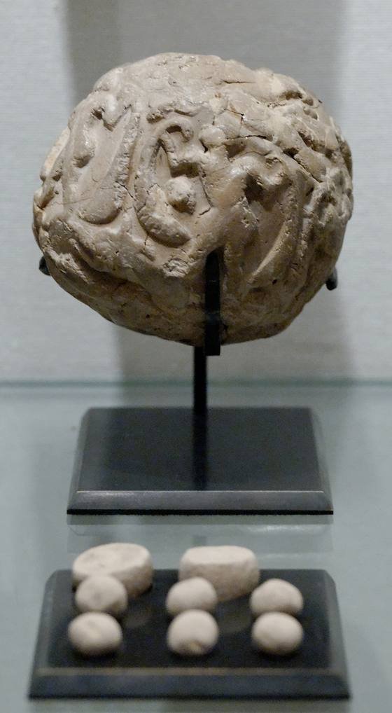 A round clay ball covered with seal impressions on a stand, with eight small clay tokens displayed below it