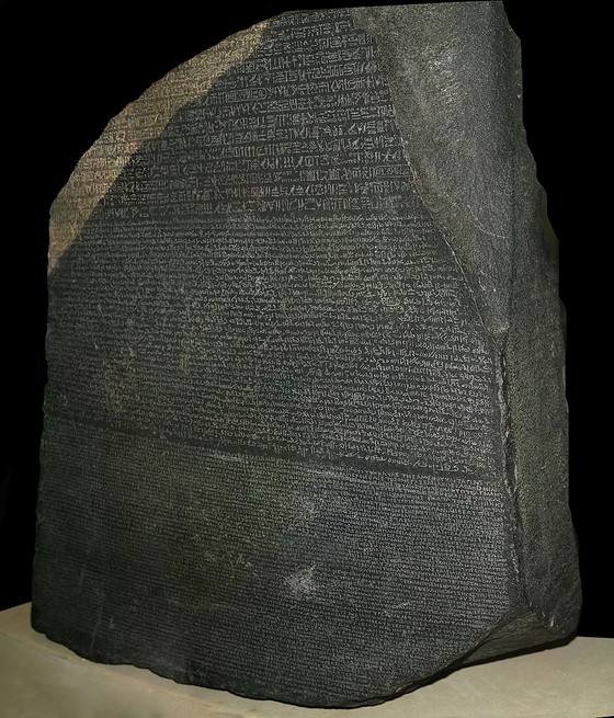 The Rosetta Stone on display: a dark gray slab with a broken top, covered in three bands of carved text
